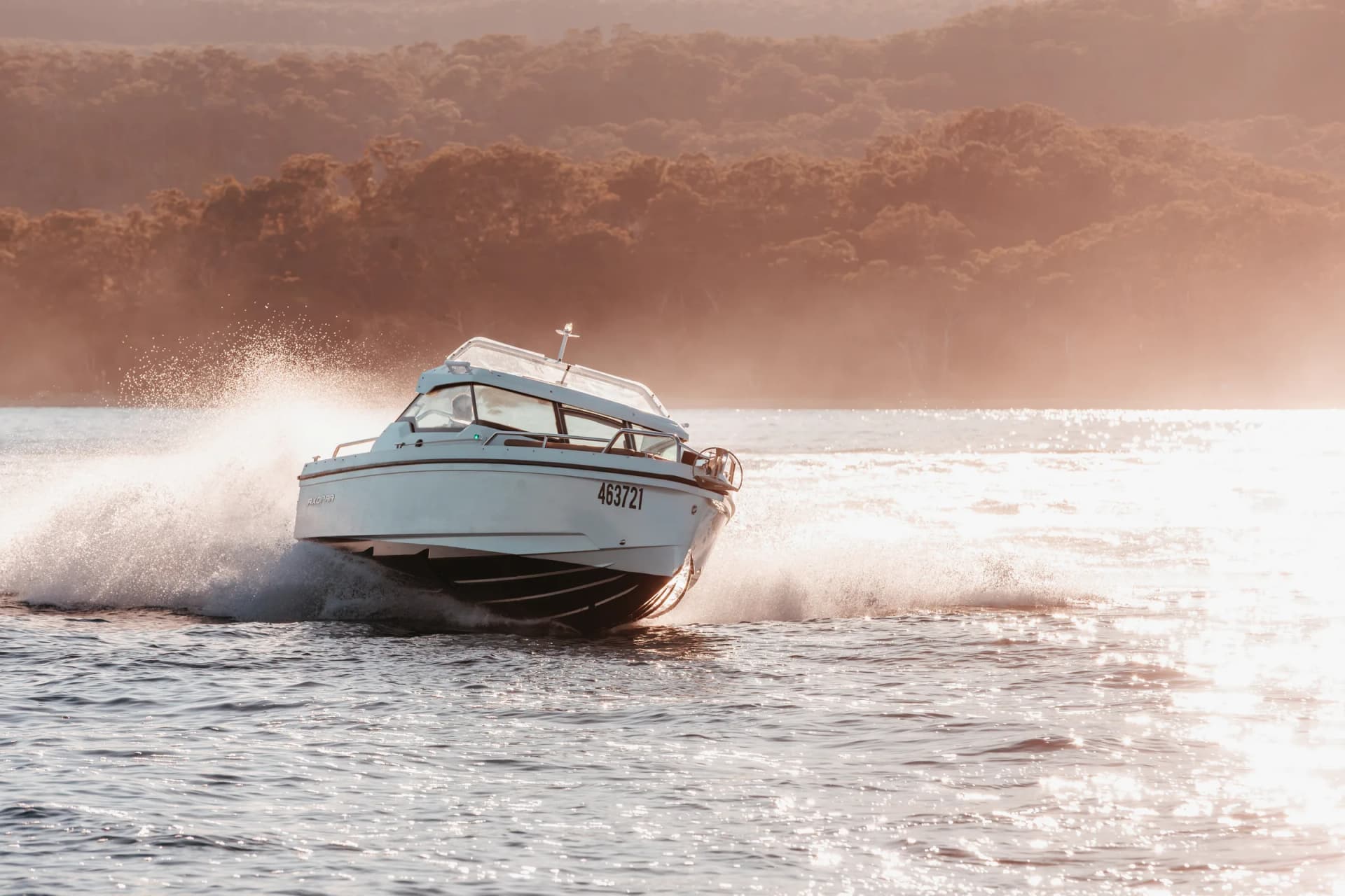 Axopar 24 HT at speed on Moreton Bay at golden hour, bushland shoreline behind