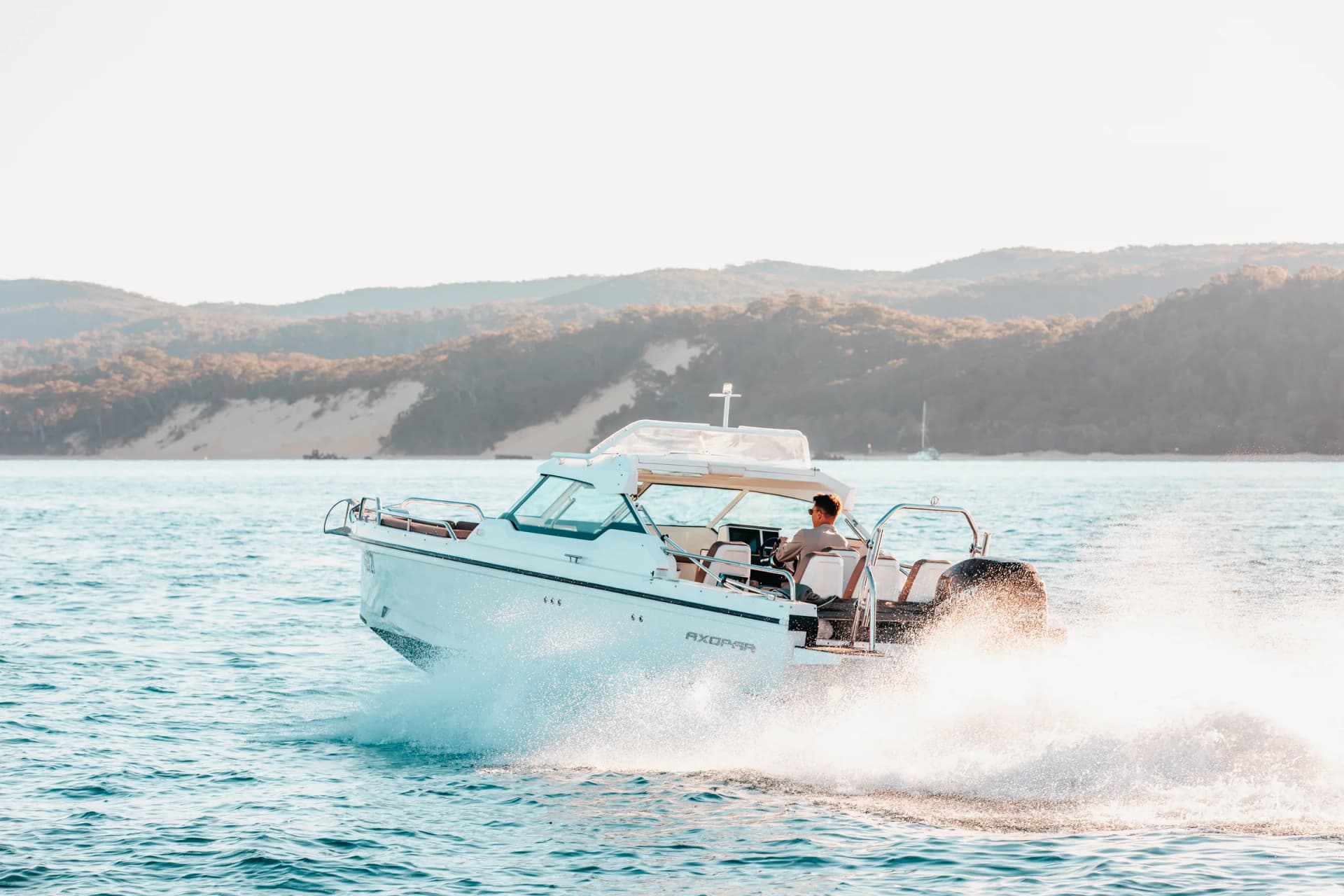 Rear quarter of Sea La Vie in a turn, spray over the wake, dunes behind