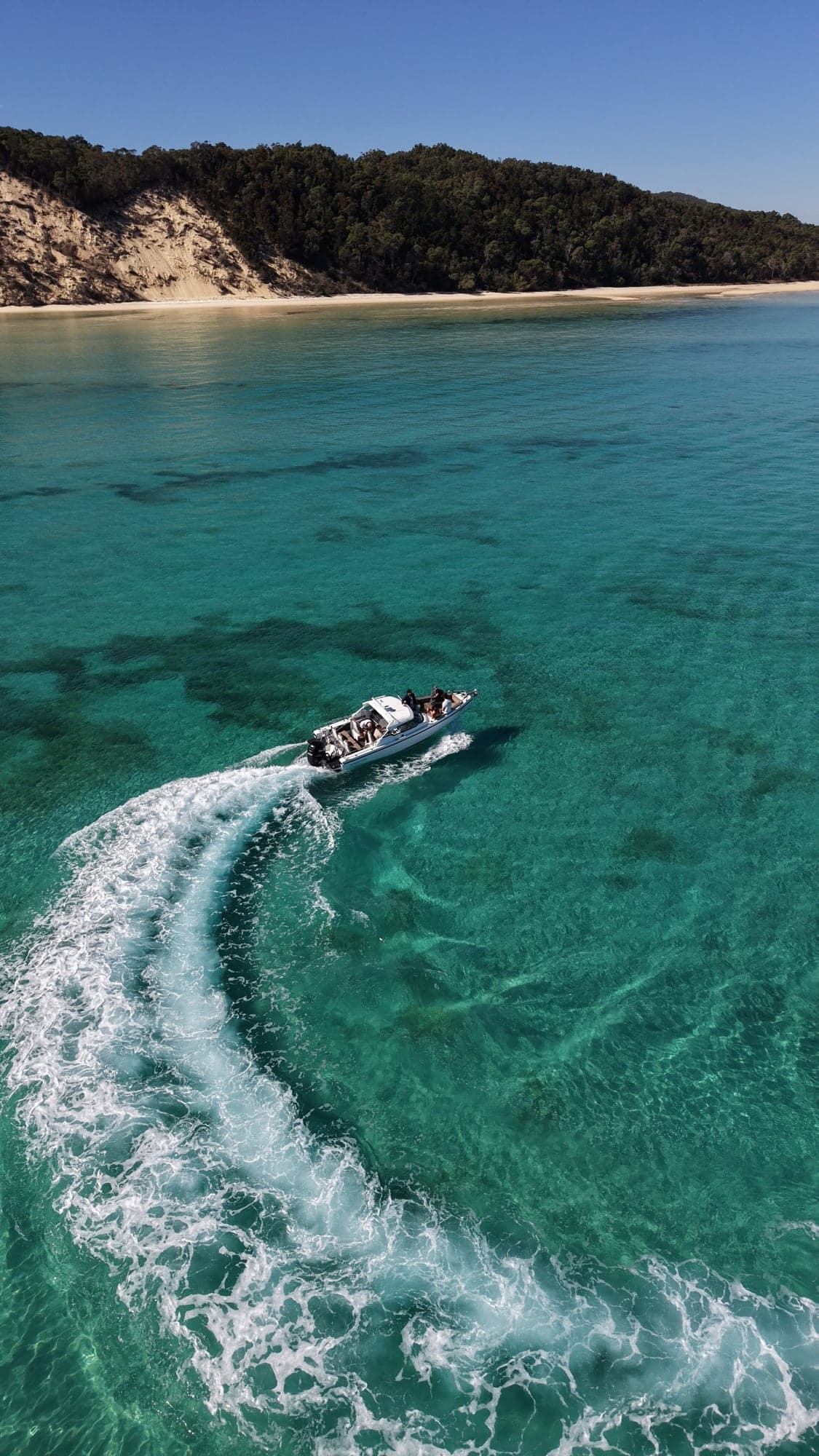 The Sea La Vie Axopar carving a white wake through clear turquoise water below the sand dunes of Moreton Island