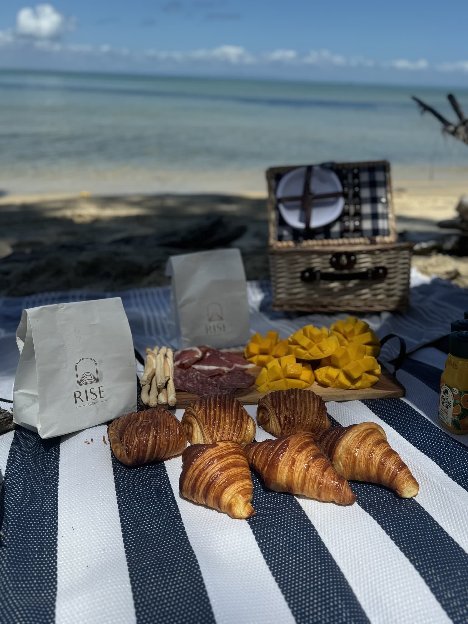 Beach picnic close-up with croissants, pain au chocolat, mango and charcuterie by the water