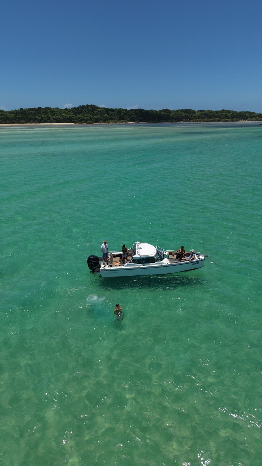 The charter boat at anchor on clear turquoise water with an island headland behind