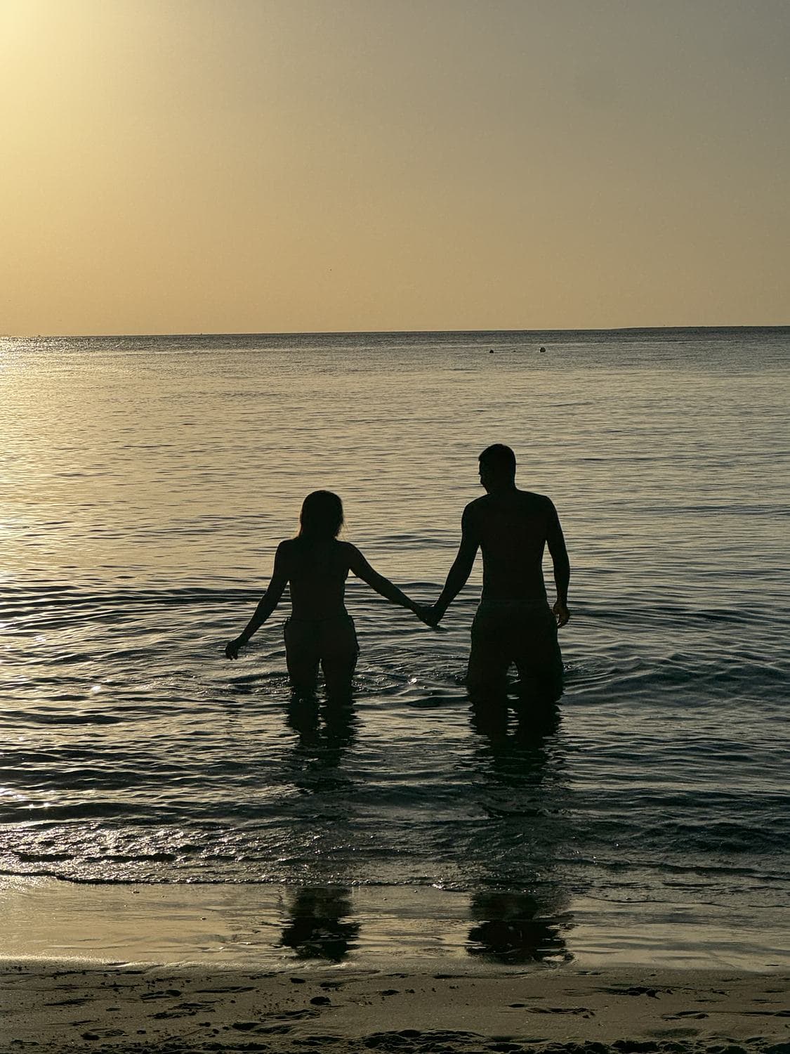 A couple silhouetted hand in hand walking into a golden sunset on the water