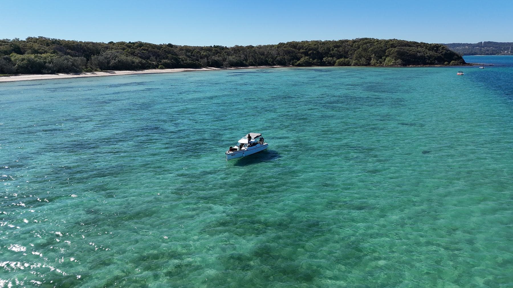 The charter boat at anchor on clear turquoise water with an island headland behind