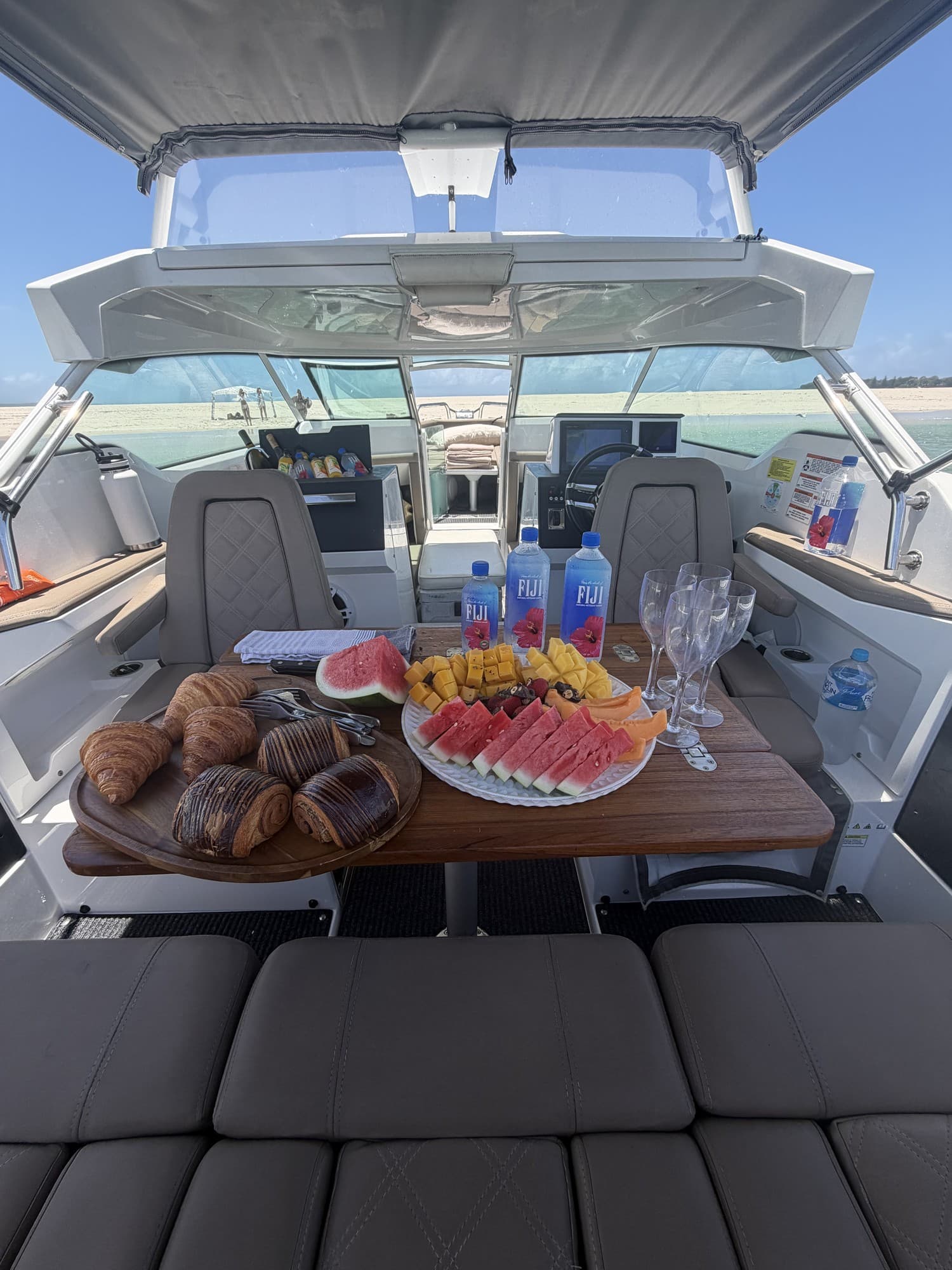 Cockpit table set with croissants, watermelon, mango and champagne flutes on the water