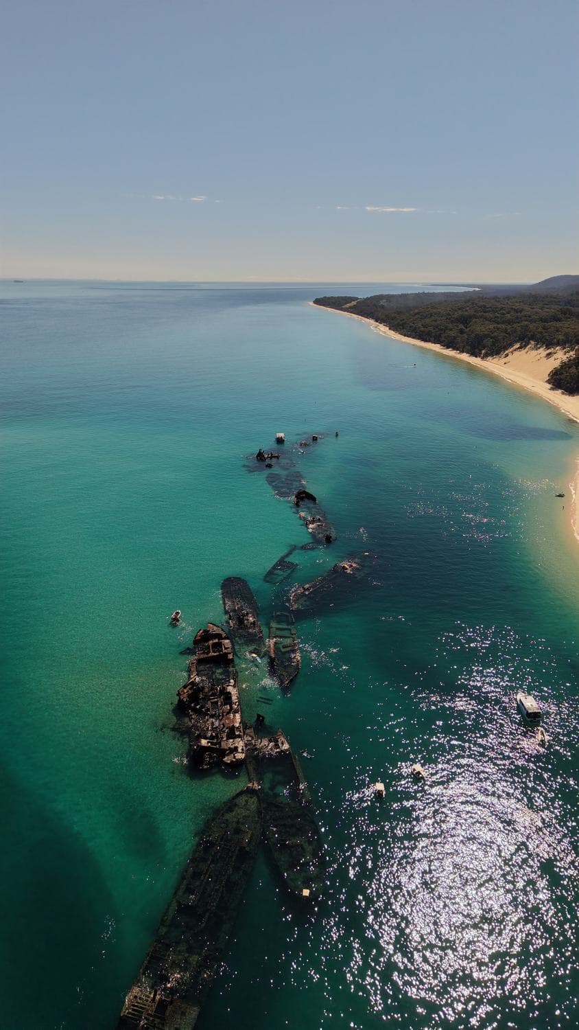 Aerial of the Tangalooma wreck line in turquoise water with snorkellers drifting below